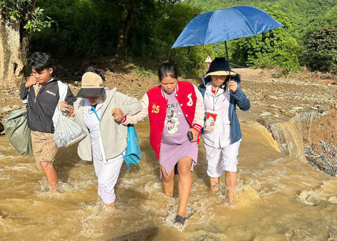 Chị Hiền (thứ hai từ phải sang), được điều dưỡng dìu qua đoạn đường sạt lở khi đi sinh con, sáng 29/7. Ảnh: Hùng Lê